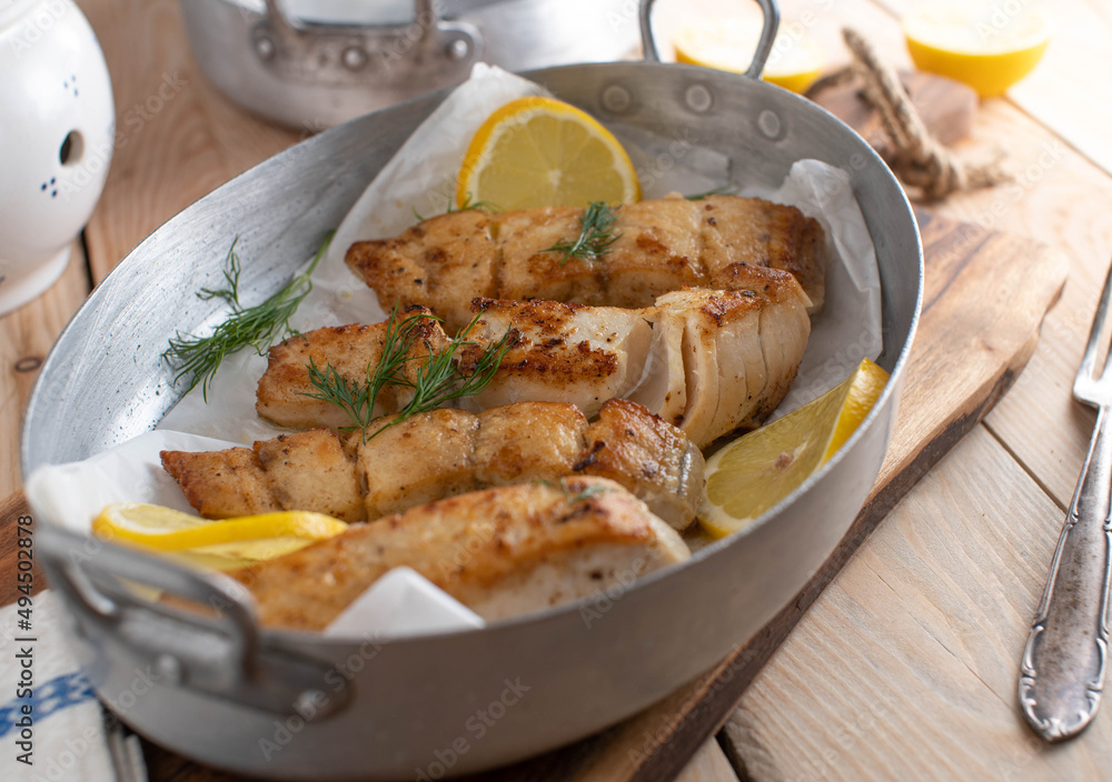 Pan fried pollock fillet with lemon and dill in a roasting pan Pan fried pollock fillet with lemon and dill in a roasting pan