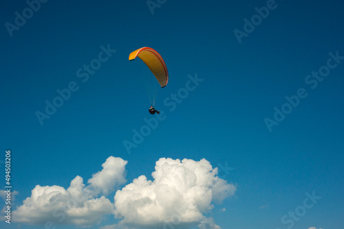 Yellow paraglider flying in the blue sky against the background of clouds. Paragliding in the sky on a sunny day.