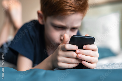 Modern technology hands of a red-haired boy child holding a mobile phone, watching cartoons or playing a video game on a smartphone