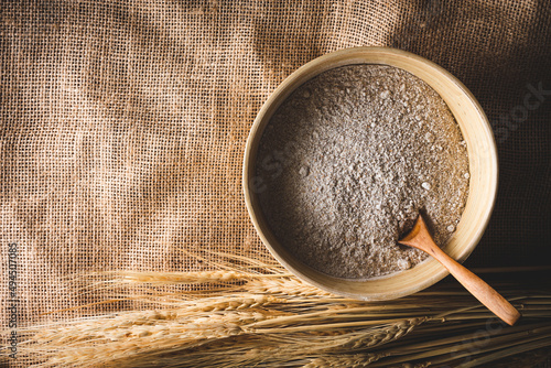 vista superior de un cuenco con harina de trigo integral, con espigas de trigo, sobre una tela de arpillera photo