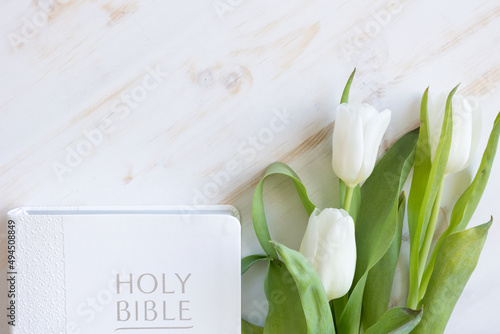 White tulips and a white christian bible on a white wood background with copy space