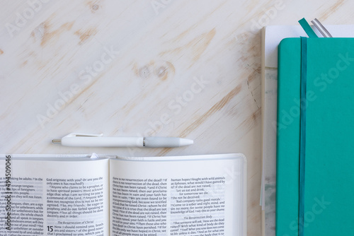 Border of open bible, teal journal and devotional and white pen on a white wood background with copy space