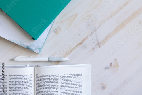 Border of open bible, teal journal and devotional and white pen on a white wood background with copy space