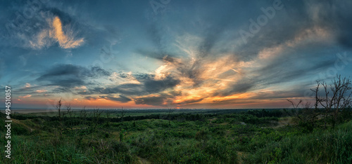 Wide-angle shot of a greenfield with the golden sun setting behind the clouds
