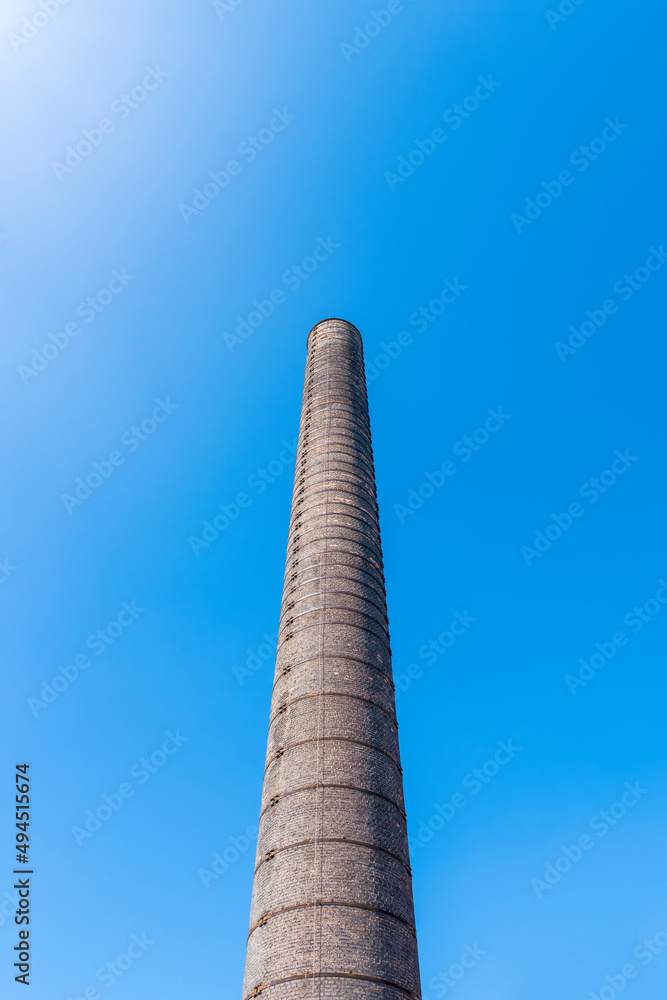 Tall, brick, industrial chimney located in Porcelain Factory (Fabryka Porcelany) in Katowice, Silesia, Poland against blue, cloudless sky.