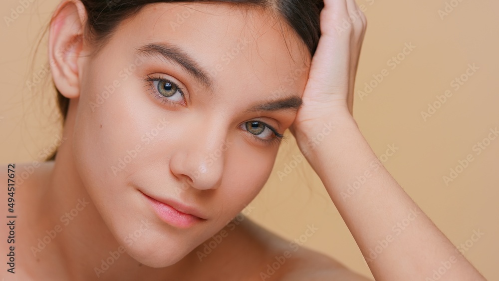 Close-up beauty portrait of young woman with pure skin who looks at camera props his head up with his hand on beige background Close-up beauty portrait of young woman with pure skin who looks at camera props his head up with his hand on beige background