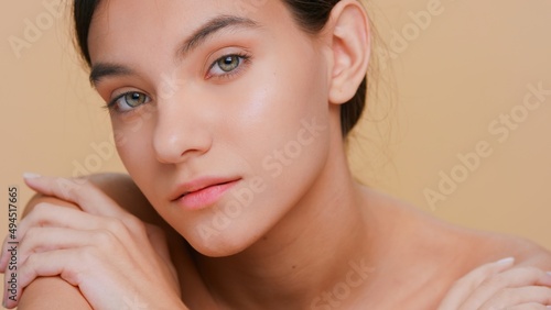 Extreme closeup beauty portrait of young brunette woman with perfect skin who softly touches her shoulders and looks at camera