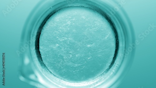 Top view macro shot of glycerin being poured into a beaker with water and dissolves in it on cyan background | Abstract body care cosmetics formulation concept