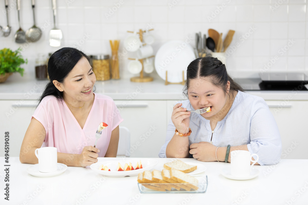 mother with down syndrome teenage girl or her daughter, eating apple together in a kitchen mother with down syndrome teenage girl or her daughter, eating apple together in a kitchen