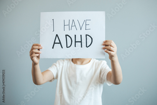 Young boy holds ADHD text written on sheet of paper. ADHD is Attention deficit hyperactivity disorder. Close up.. Attention Deficit Hyperactivity Disorder or ADHD