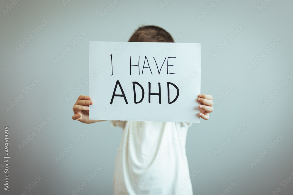 Young boy holds ADHD text written on sheet of paper. ADHD is Attention deficit hyperactivity disorder. Close up. Attention Deficit Hyperactivity Disorder or ADHD Young boy holds ADHD text written on sheet of paper. ADHD is Attention deficit hyperactivity disorder. Close up. Attention Deficit Hyperactivity Disorder or ADHD