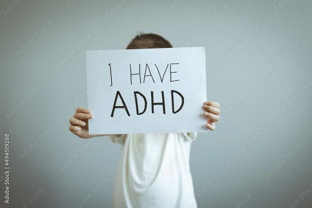 Young boy holds ADHD text written on sheet of paper. ADHD is Attention deficit hyperactivity disorder. Boy holding blackboard and admitting suffering from ADHD Young boy holds ADHD text written on sheet of paper. ADHD is Attention deficit hyperactivity disorder. Boy holding blackboard and admitting suffering from ADHD