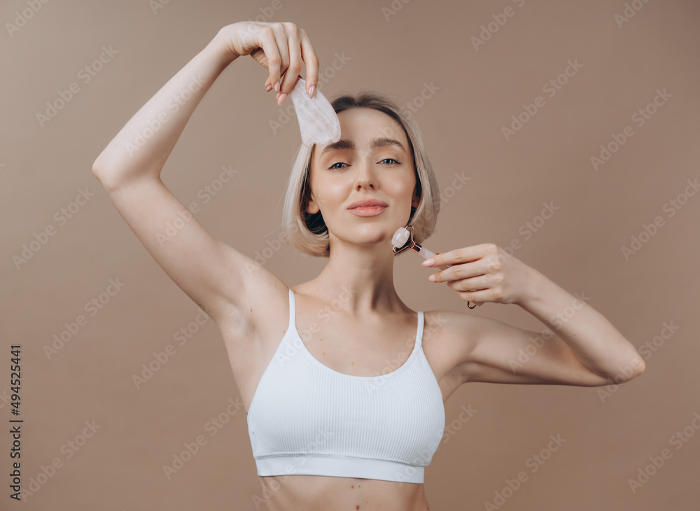 Woman with face roller and jade gua sha stone. Young model advertising skin rejuvenation products. Concept of beauty and self care. Woman with face roller and jade gua sha stone. Young model advertising skin rejuvenation products. Concept of beauty and self care.