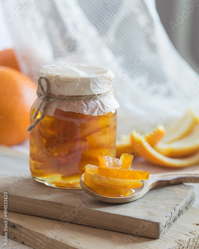 Homemade candied peels orange confiture in glass jar on light background, selective focus