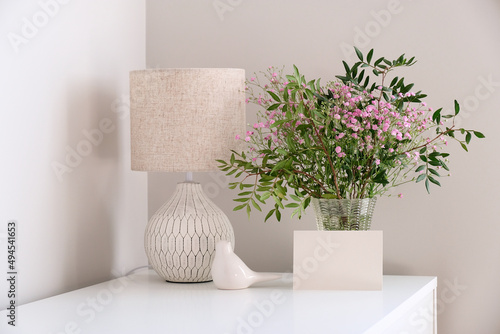Cozy home desk table with lamp, bunch of spring flowers in vase, greeting card mockup. Hygge, boho style, scandinavian living room