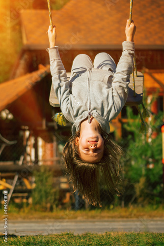 Young beautiful girl hanging upside down and having fun on a swing outdoor. Happy childhood  summer vacation  holiday and rest concept. Vertical image.