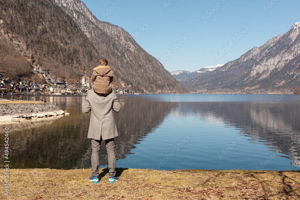 Father and son enjoying mountains, snow, lake, good weather, blue sky, sun. Little boy and his father spending time together. Family time. Beautiful landscape. Tourism, holiday, travel. Amazing view.