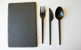 A black slate plate with eating utensils. An empty sushi plate on a white table.