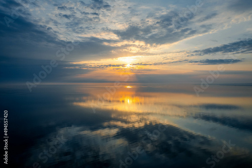 An aerial view of a beautiful sunrise through clouds reflected onto the glassy water of Lake Ontario in the early morning, in Burlington, Ontario, Canada.