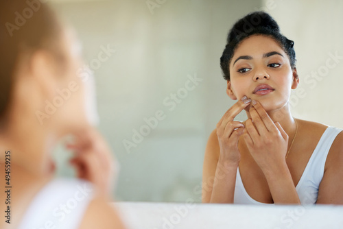 Her morning makeover. Shot of a young woman inspecting her skin in front of the bathroom mirror.