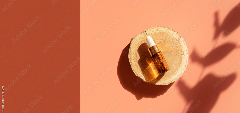 Amber glass dropper bottle on woodcut in the sunlight with eucalyptus flower shadows. Top view. Luxury and natural cosmetics presentation. Testers, beauty samples perfumery concept. Web banner