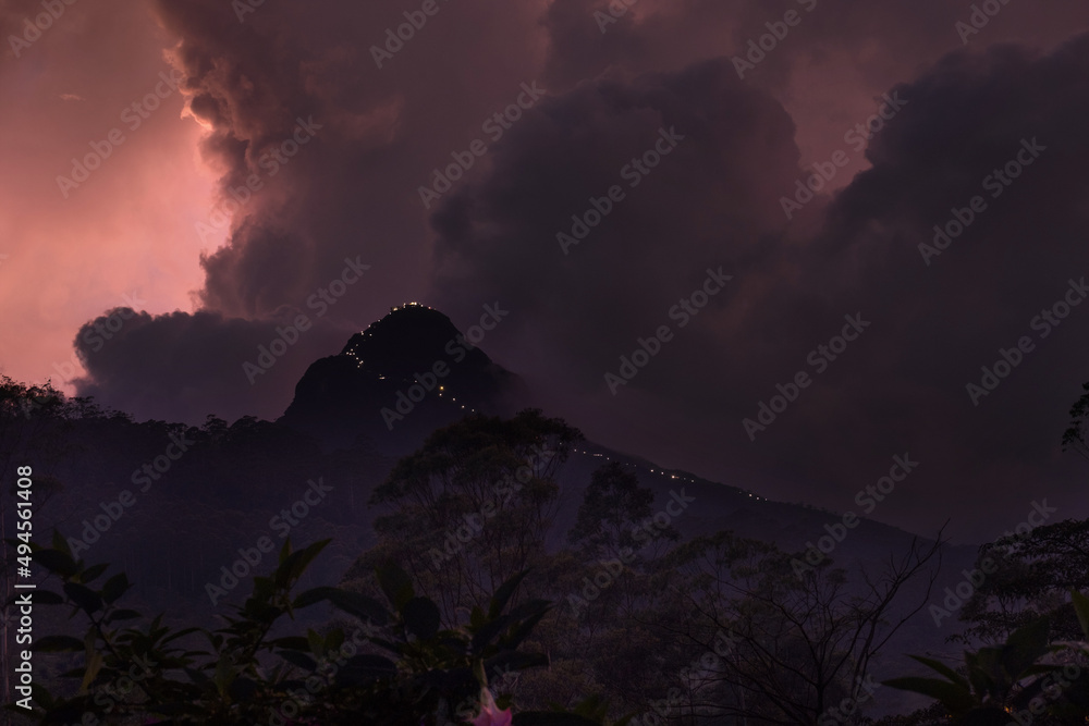 Adam's Peak is a 2243 m tall conical mountain located in central Sri Lanka - Sacred Mountain for four religions with a temple on the top. Twilight mountain photo with lights leading to the holy top.