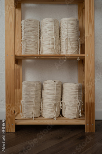 Rope of natural color for weaving macrame products. The material in the bobbins is on a wooden rack.