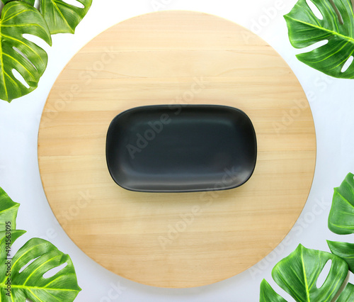 Top view of the black dish plate placed on a round wooden table with monstera palm leaves photo