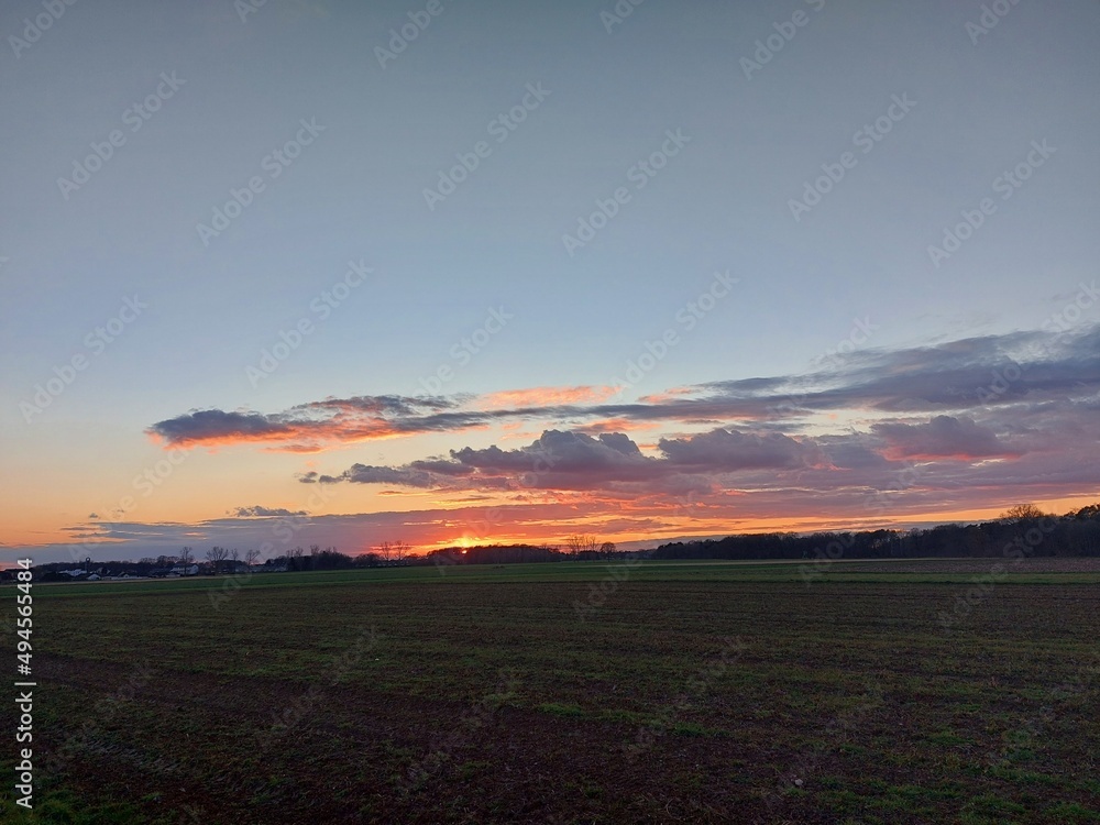 Obraz premium Herrlicher Sonnenuntergang. Die Natur versinkt in Dunkelheit. In der Ferne sieht man Silhouetten von verzweigten Laubbäumen ohne Blätter. Das Tageslicht verblasst am Horizont. Die Dunkelheit im Morgen