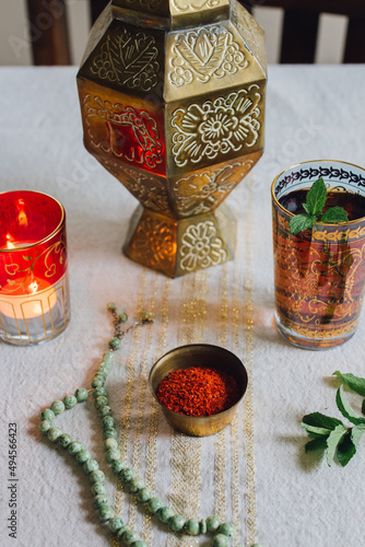 table setting with gold cloth, Aleppo chili pepper flakes in dish, tealight candle, jade prayer beads, mint tea photo