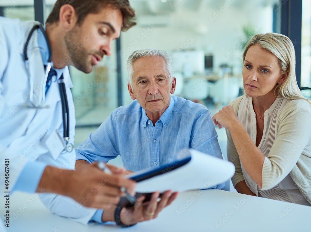 Ive got the test results right here. Shot of a doctor discussing some paperwork with a senior patient and his daughter in a clinic. Ive got the test results right here. Shot of a doctor discussing some paperwork with a senior patient and his daughter in a clinic.
