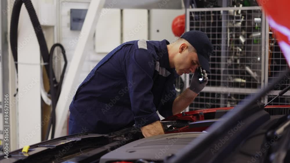 Car service worker examinating engine under hood with flashlighter in hand, side view Car service worker examinating engine under hood with flashlighter in hand, side view