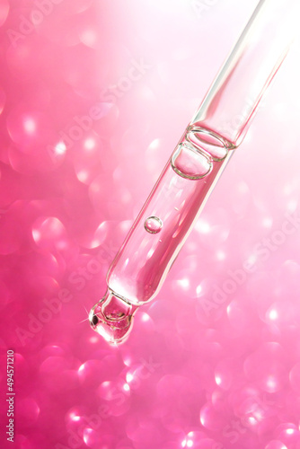 Transparent facial serum pipette on pink glitter bokeh background. Cosmetic Beauty product closeup.