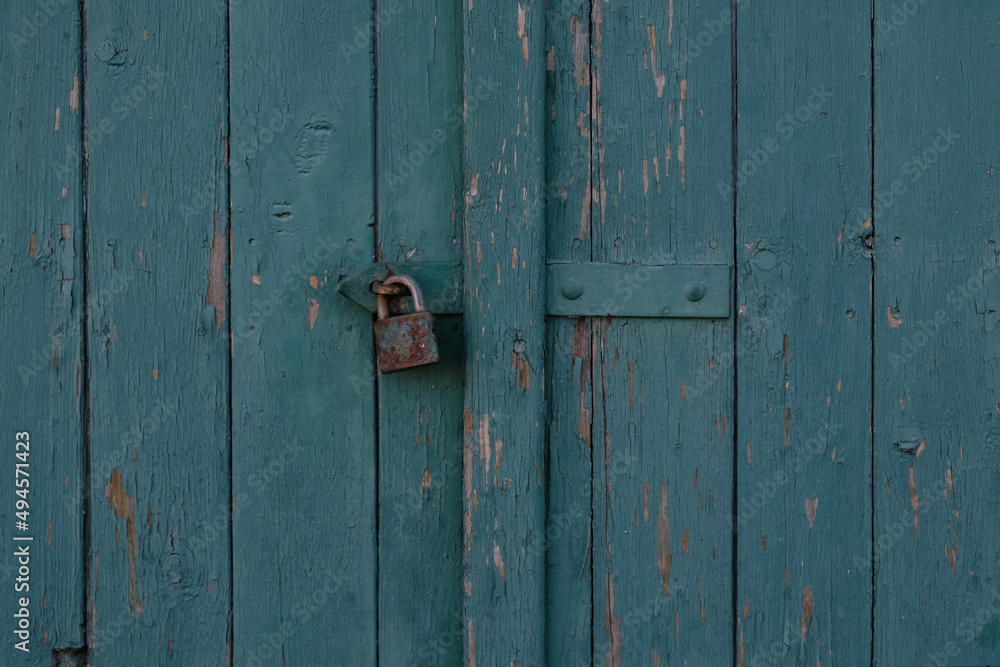 Vintage blue wooden painted door of old building. Shabby door boards. Old peeling painted door, crumbles. Rusty metal lock on the door. Threadbare Wooden rustic background. 