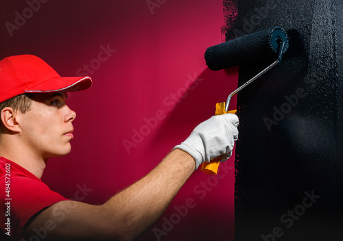Male decorator painting a wall with black color.