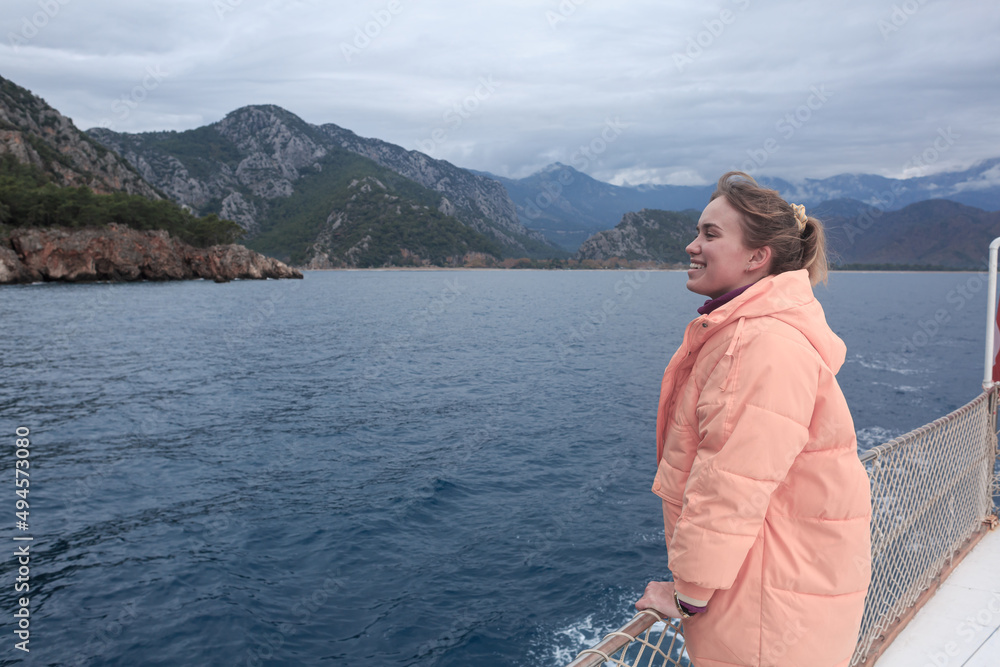 Fototapeta premium The girl is sailing on a ship in the Mediterranean Sea against the backdrop of mountains and looks into the distance. Antalya, Turkey, travel by ship.