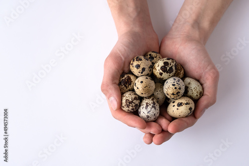 Close-up of fresh quail eggs in male hands on white background. Top view. Home cooking. Idea of healthy breakfast, symbol of Easter. Copy space