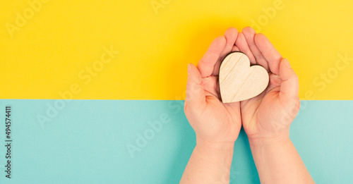 Woman is holding a heart in her hand  blue and yellow colored background  copy space  love and charity symbol  hope concept 