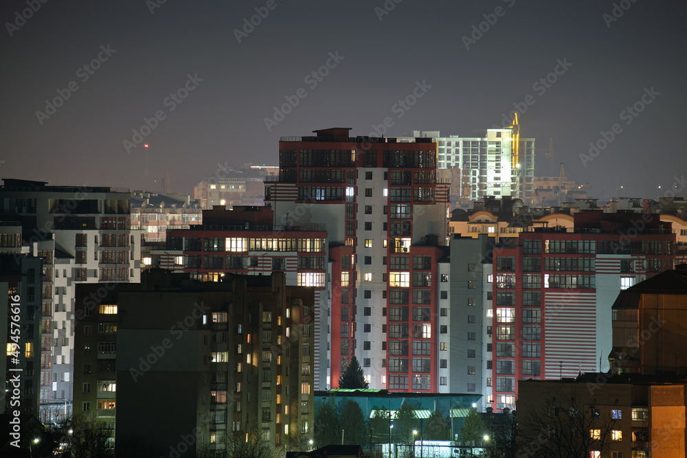 Architectural details of modern high apartment buildings with many illuminated windows and balconies at night