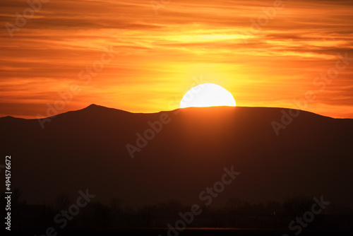 Beautiful evening panoramic landscape with bright setting sun over distant mountain peaks at sunset