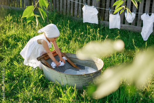 Fotografía Sweet girl in a kerchief and a dress launder snow-white linen by hand on an old washing board