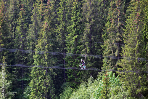 A young man rides a ride on a bicycle on ropes above the ground. Against the background of green trees