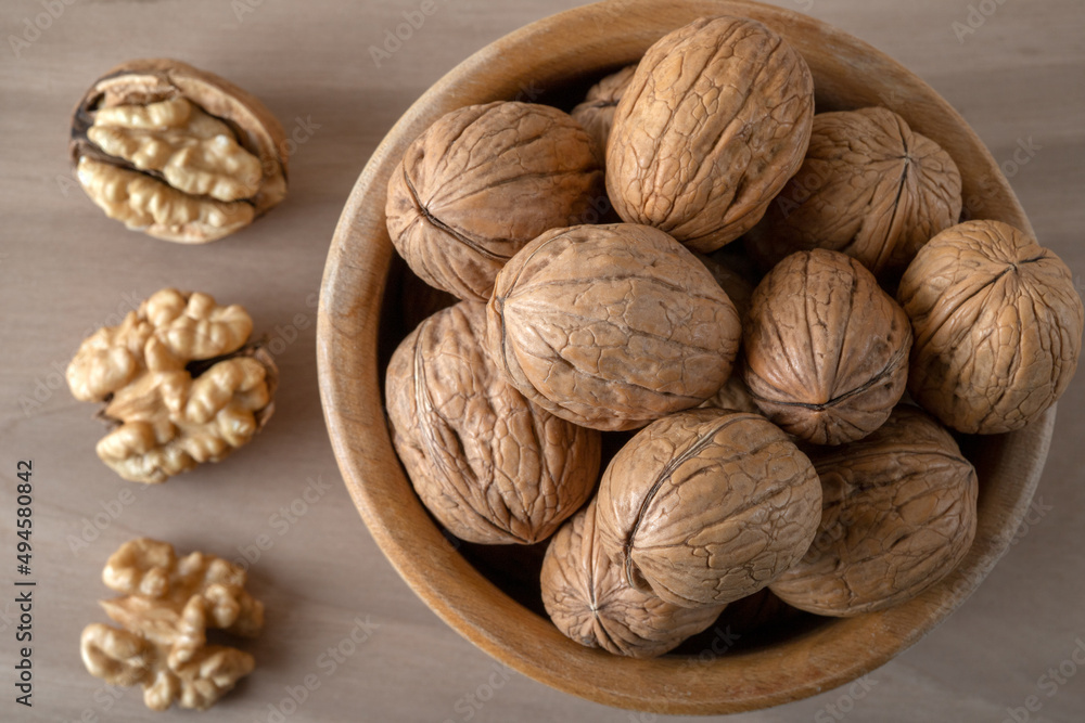 Walnut kernels and whole walnuts in bowl on wooden background Walnut kernels and whole walnuts in bowl on wooden background