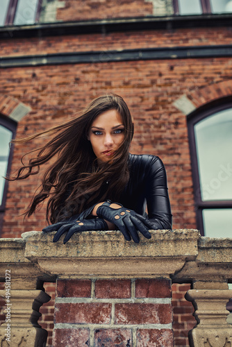 Giving you a piercing gaze. Seductive young woman in a black catsuit looking at you from a rooftop. photo