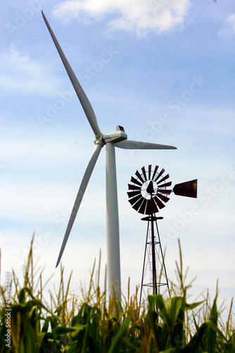 An old water pumping windmill stands in contrast to the giant energy producing wind turbine  on a wind farm near Fowler, Indiana, USA. They are located in a cornfield.