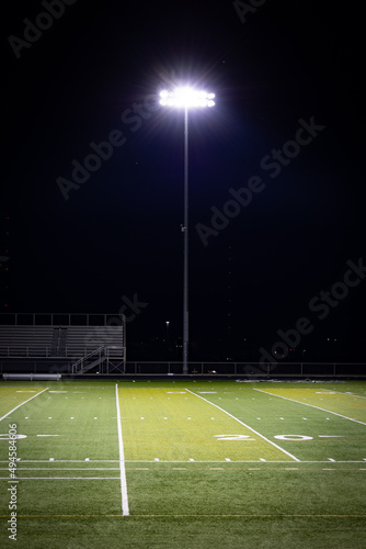 Stadium lights on a poll next to American football high school field with artificial grass surface