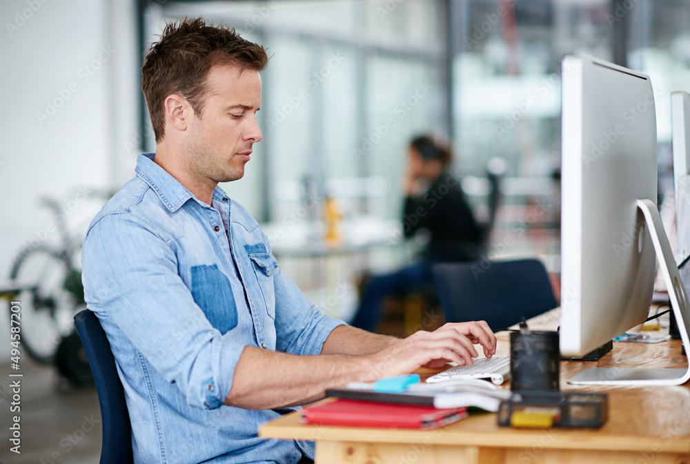 He wont stop until he gets the job done. Shot of a handsome young man working at his desk in an office. He wont stop until he gets the job done. Shot of a handsome young man working at his desk in an office.