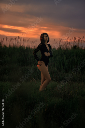 A beautiful girl in a bodysuit against the backdrop of nature and a beautiful sunset