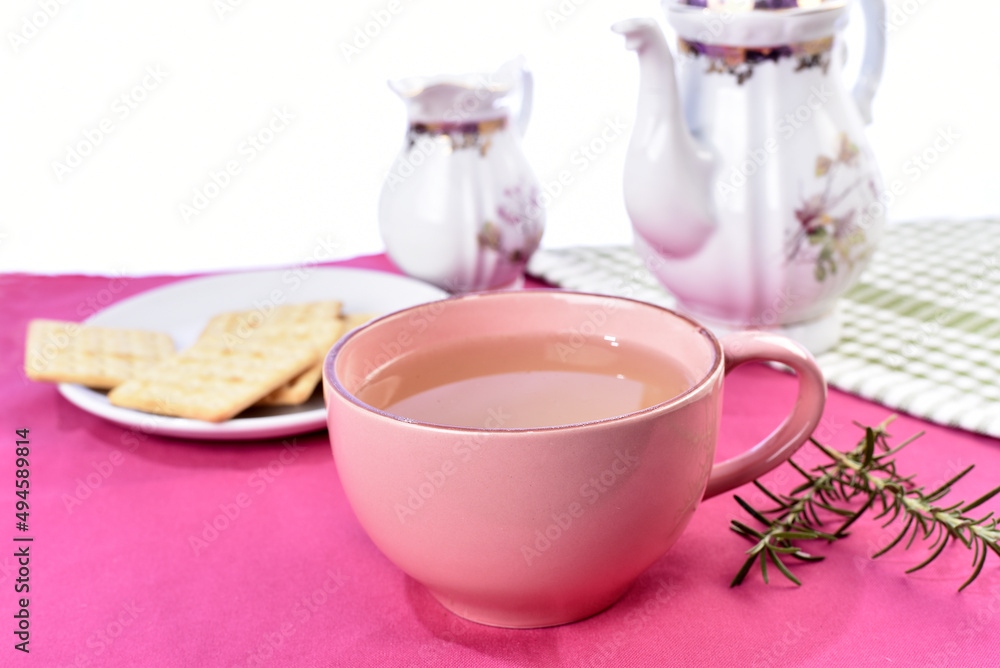 pink cup with lemon balm green tea, crackers old porcelain teapot in the background pink cup with lemon balm green tea, crackers old porcelain teapot in the background
