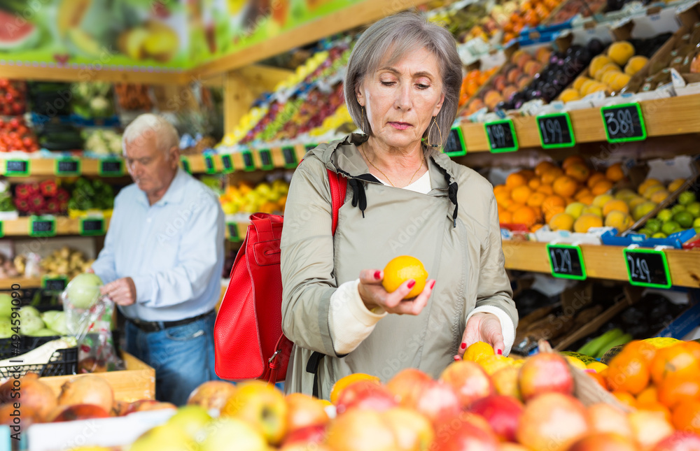 Mature woman selecting tangerines in supermarket. Senior man shopping in background.